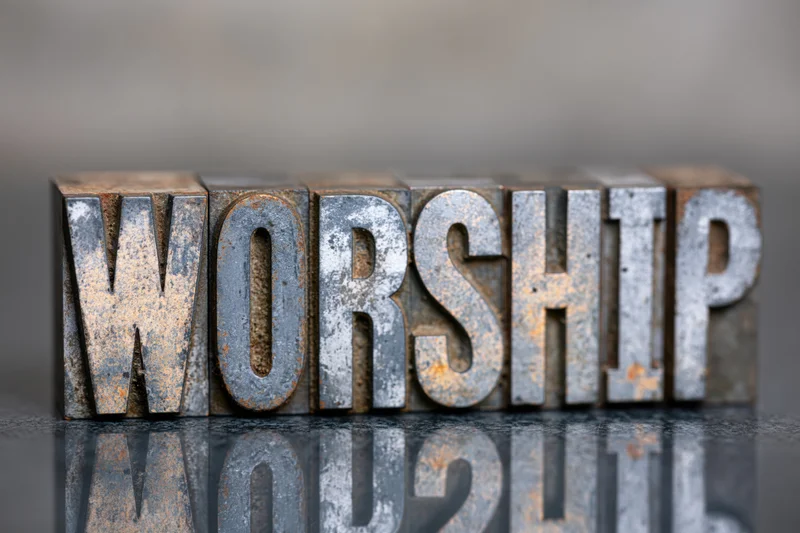 Antique metal letterpress blocks spelling worship arranged in a row on a reflective surface