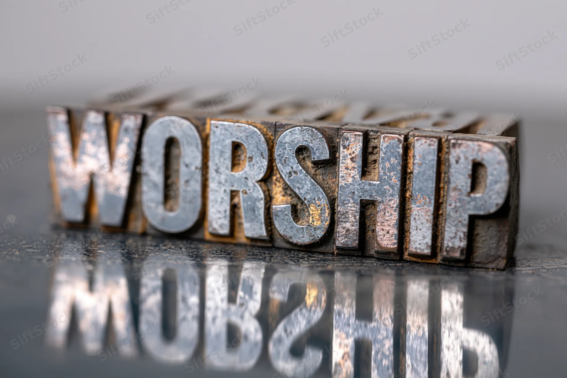 Antique metal letterpress blocks spelling worship arranged on a reflective surface