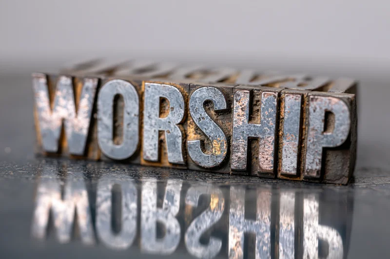 Antique metal letterpress blocks spelling worship arranged on a reflective surface