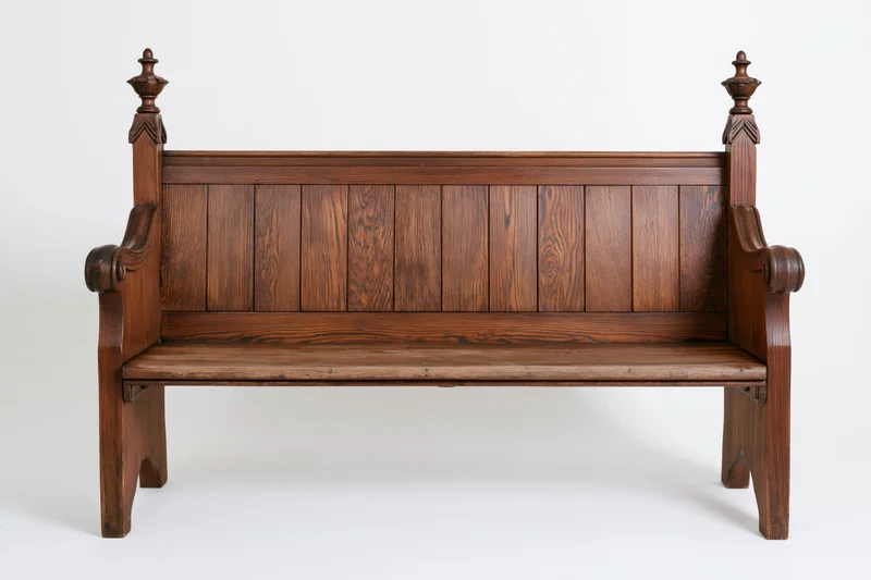Antique wooden church pew with vertical plank backrest and carved finials, isolated on white background