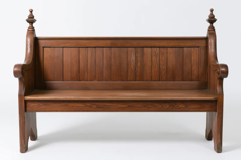 Antique wooden church pew with vertical plank backrest and carved armrests on white background