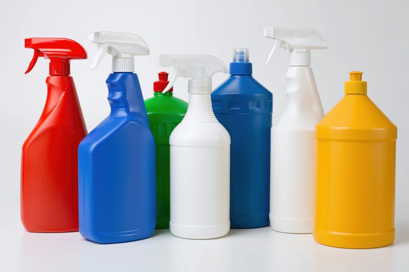Assorted cleaning product bottles with spray nozzles arranged in a row on a white surface
