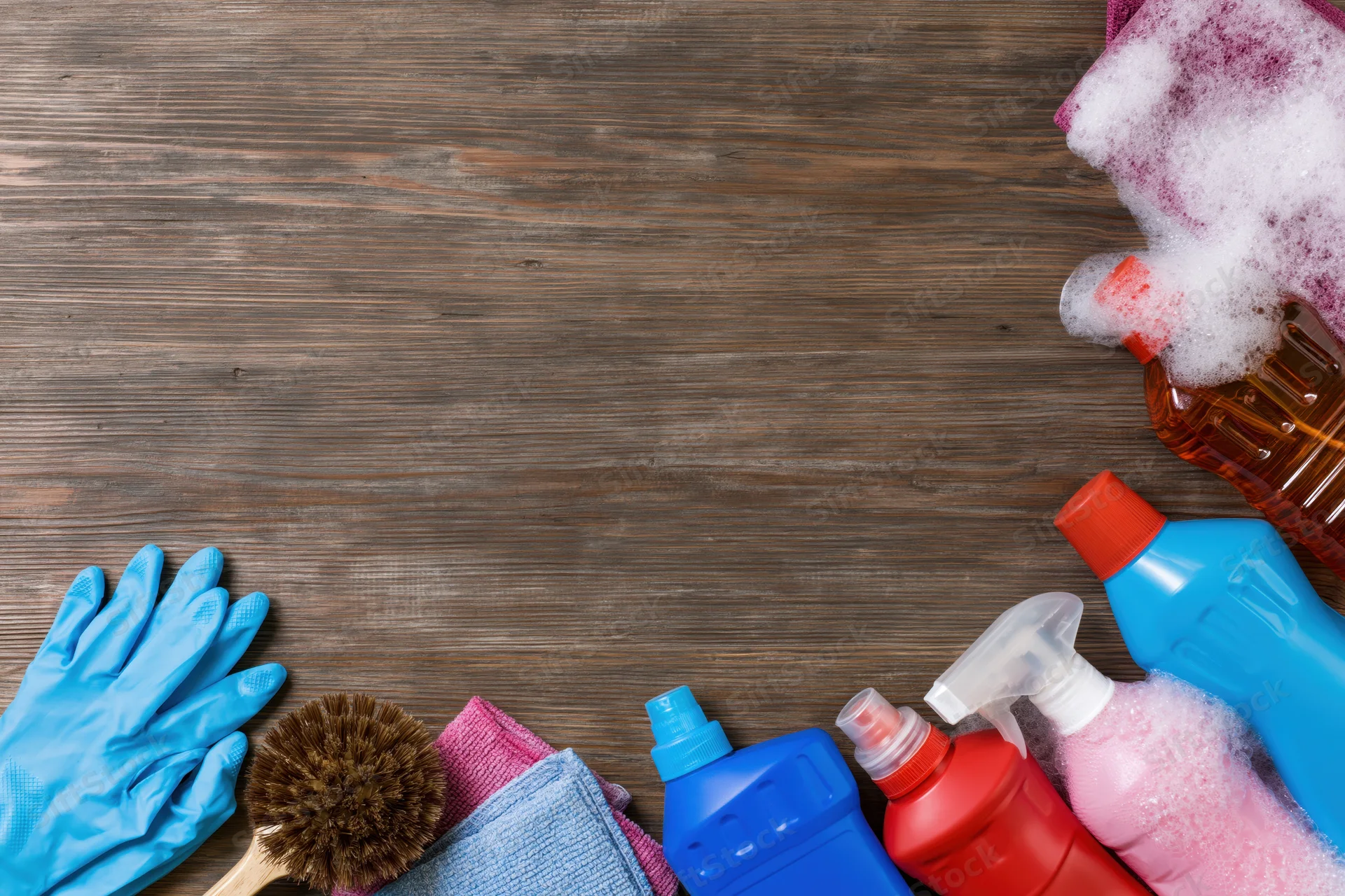 Cleaning supplies arranged along the bottom edge of a wooden surface with copyspace above