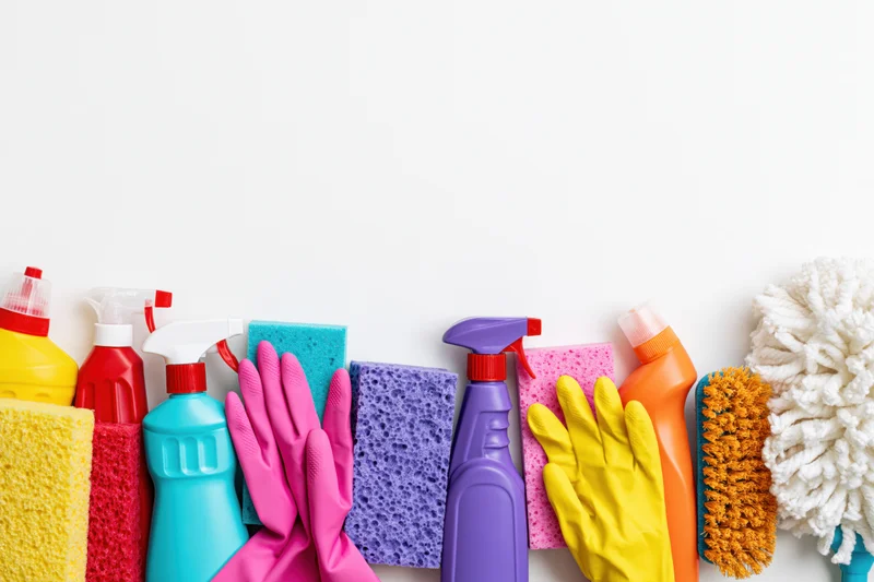 Colorful household cleaning supplies arranged in a row on white background with copyspace