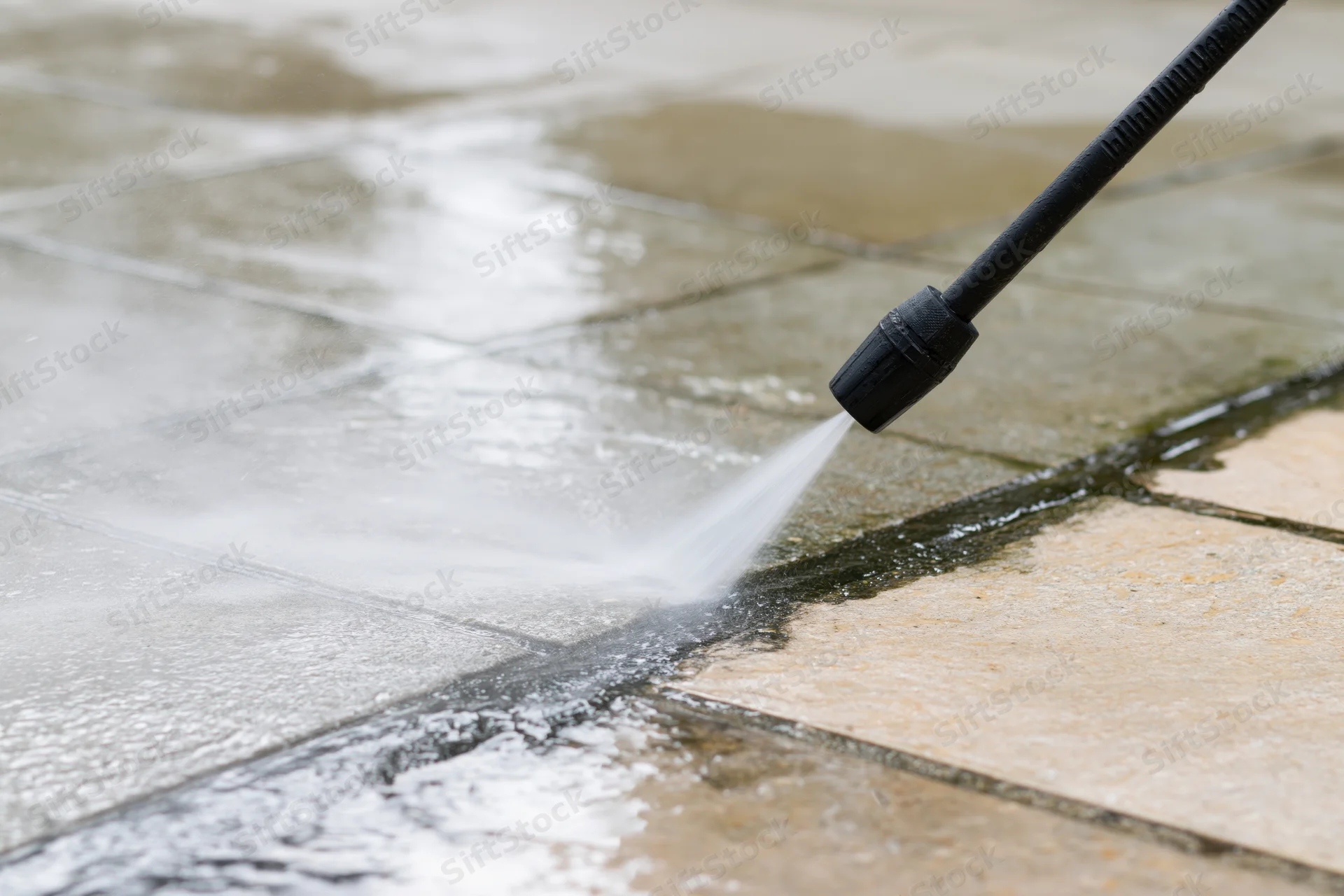 Pressure washer wand spraying water onto a tiled patio surface