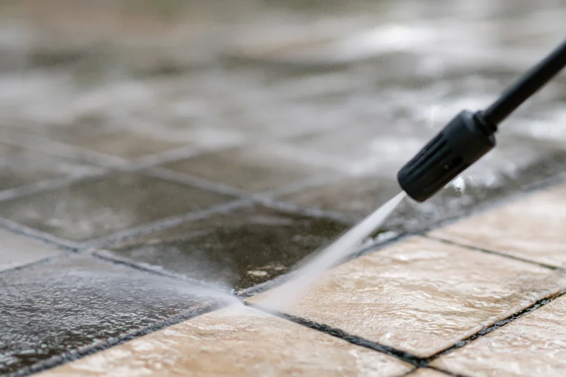 Pressure washer nozzle spraying water onto tiled patio surface