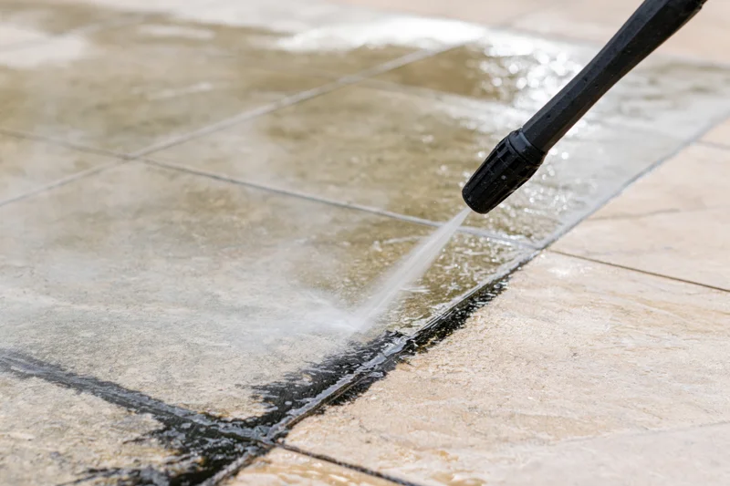 Pressure washer nozzle spraying water onto tiled patio surface
