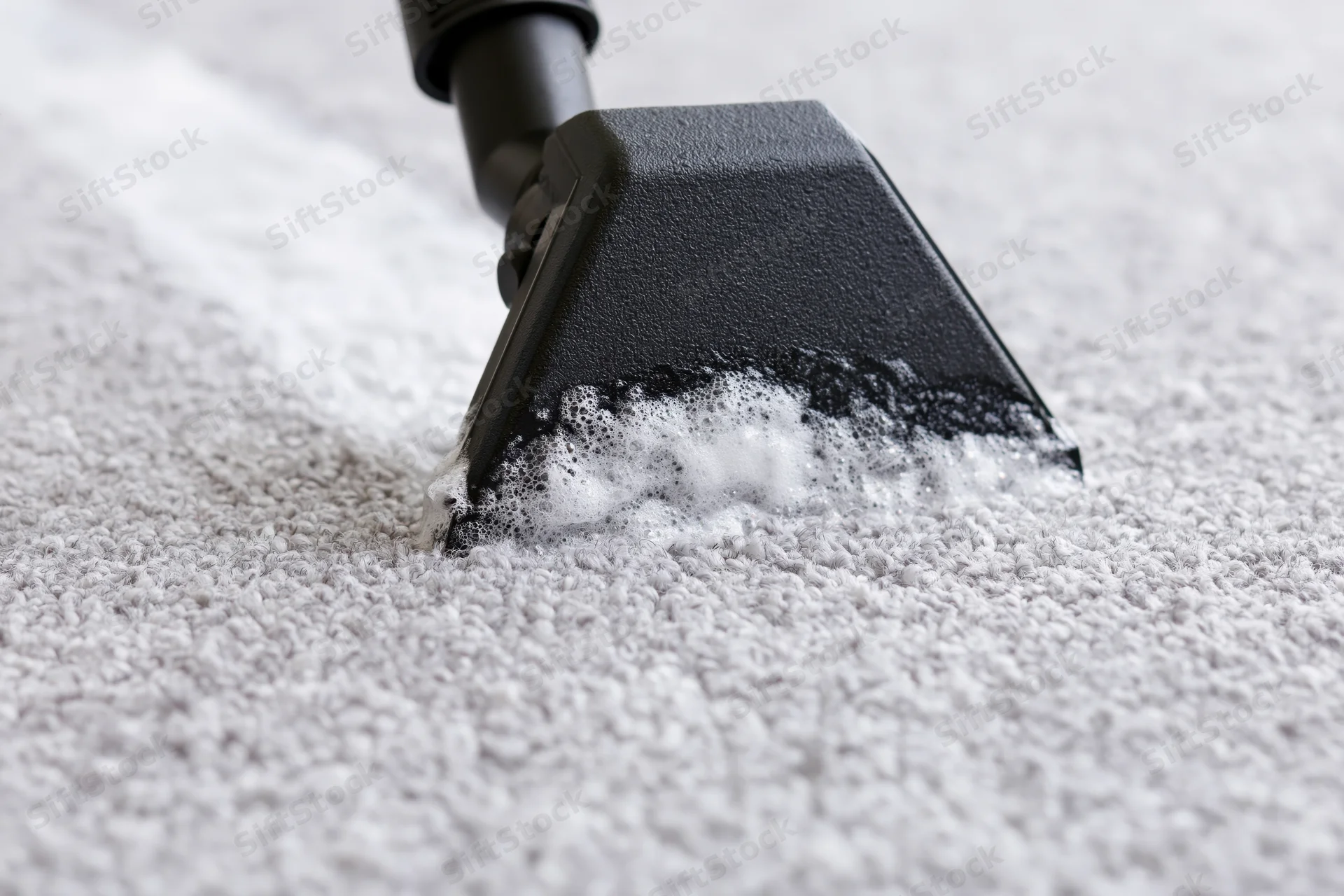 Black triangular vacuum nozzle extracting foam from white carpet