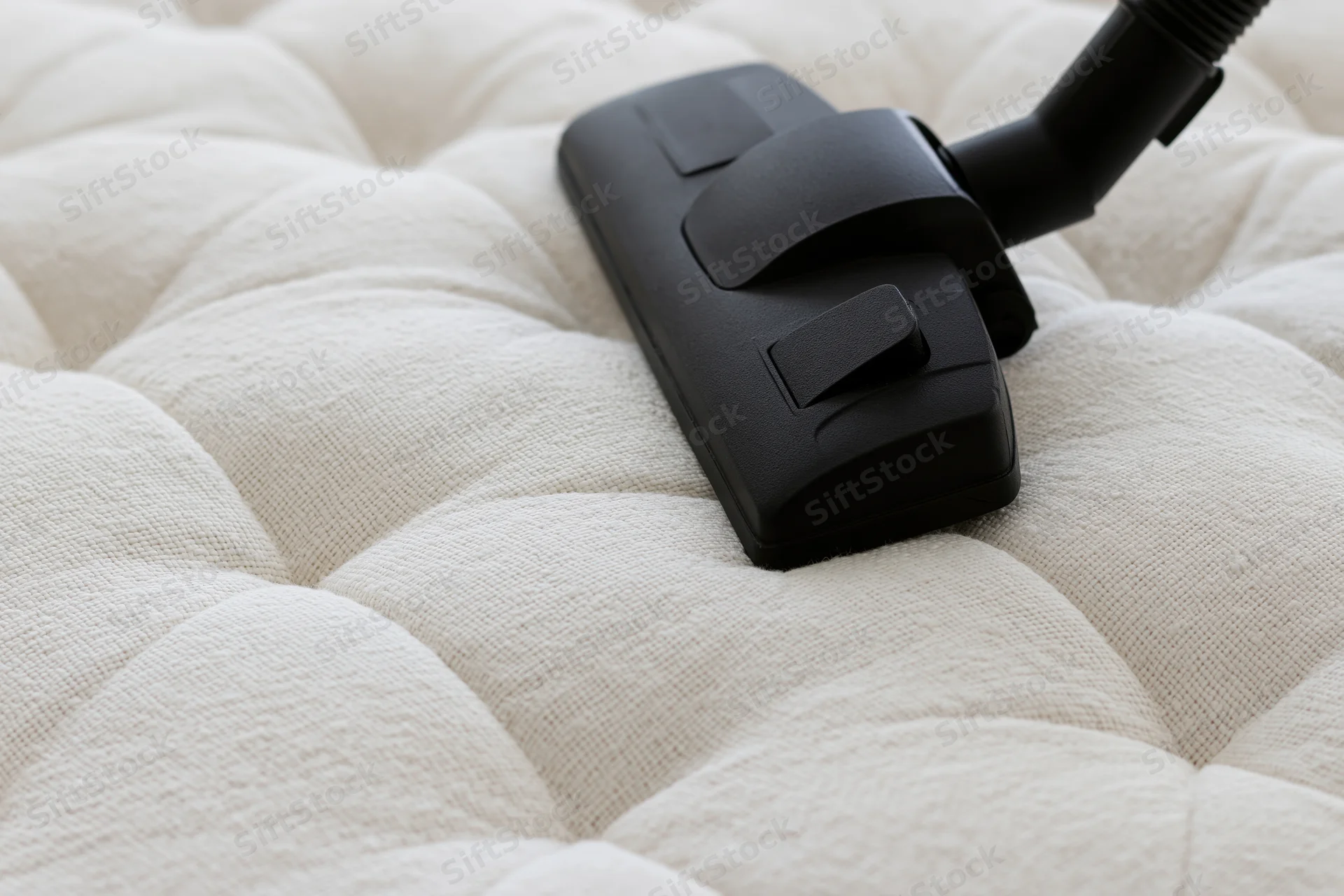 Black vacuum attachment on tufted white mattress surface