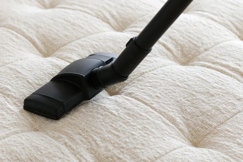 Black vacuum attachment cleaning a tufted mattress surface
