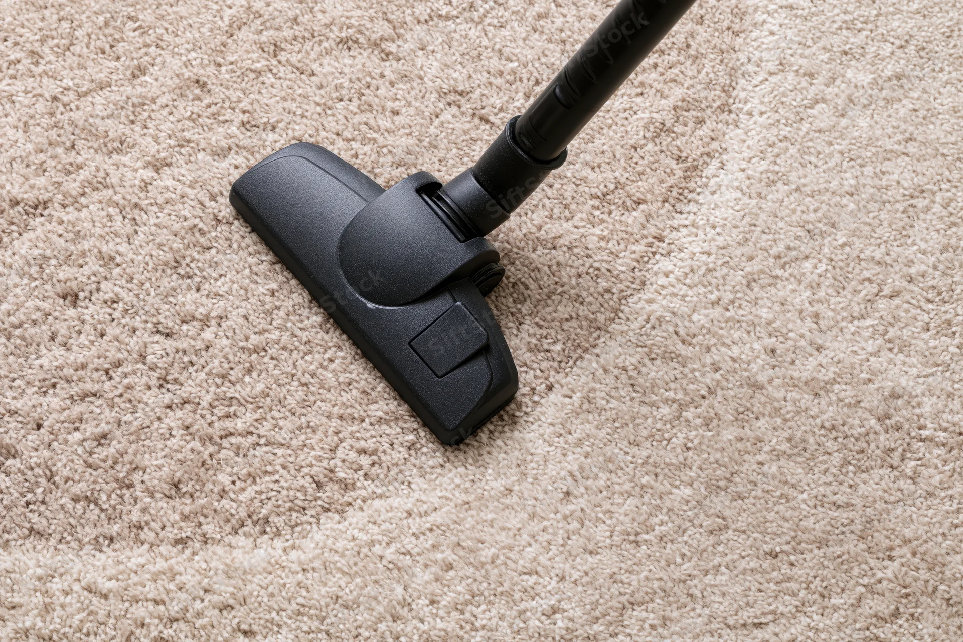 Black vacuum cleaner head moving across beige-brown carpet
