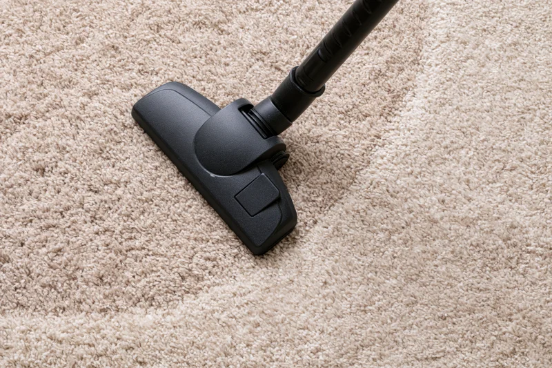 Black vacuum cleaner head moving across beige-brown carpet
