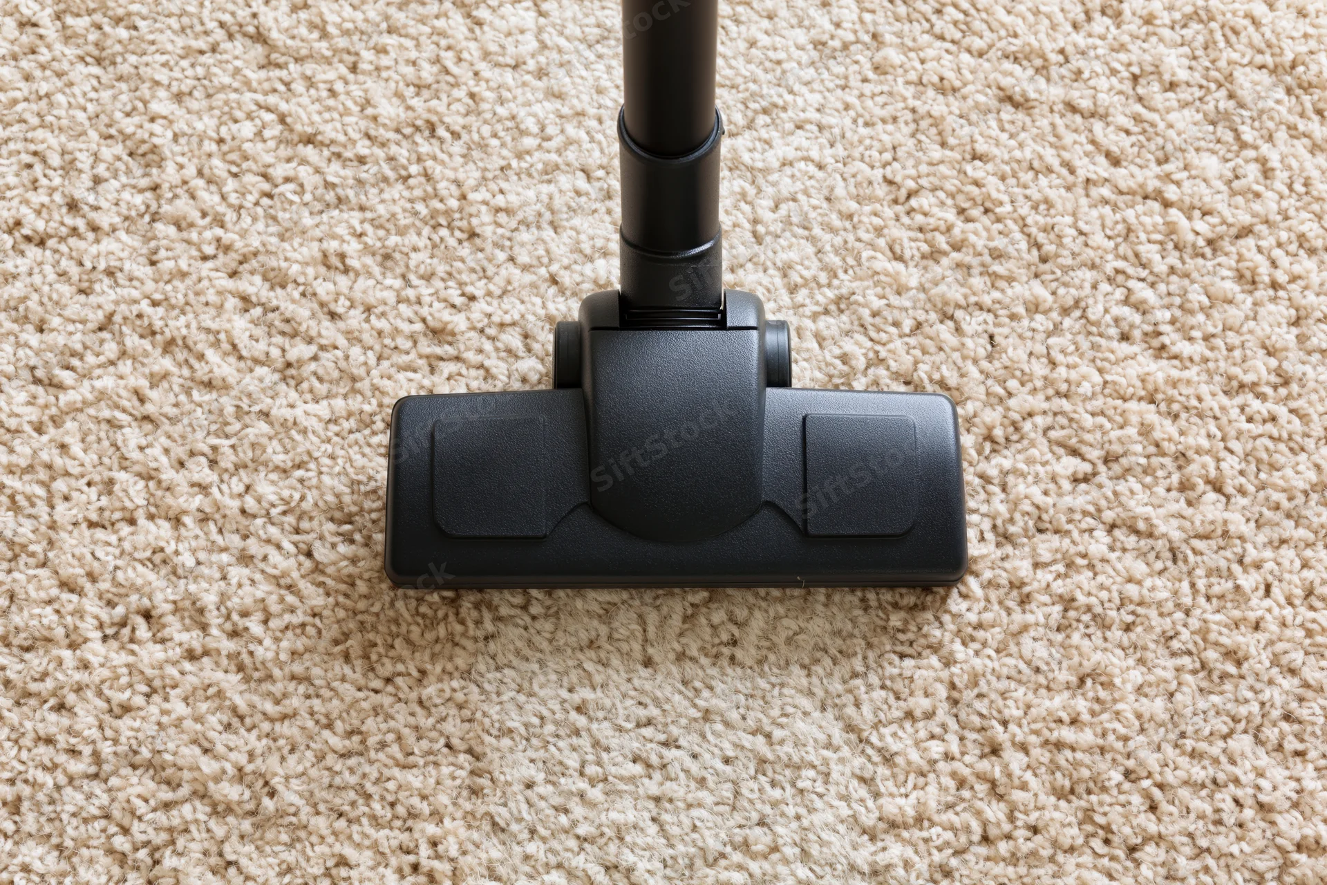 Vacuum cleaner head moving across beige carpet in home interior