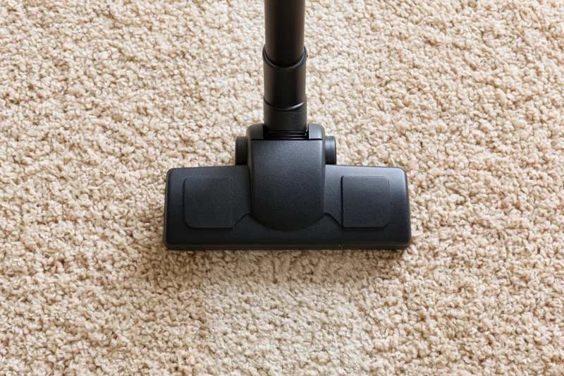 Vacuum cleaner head moving across beige carpet in home interior