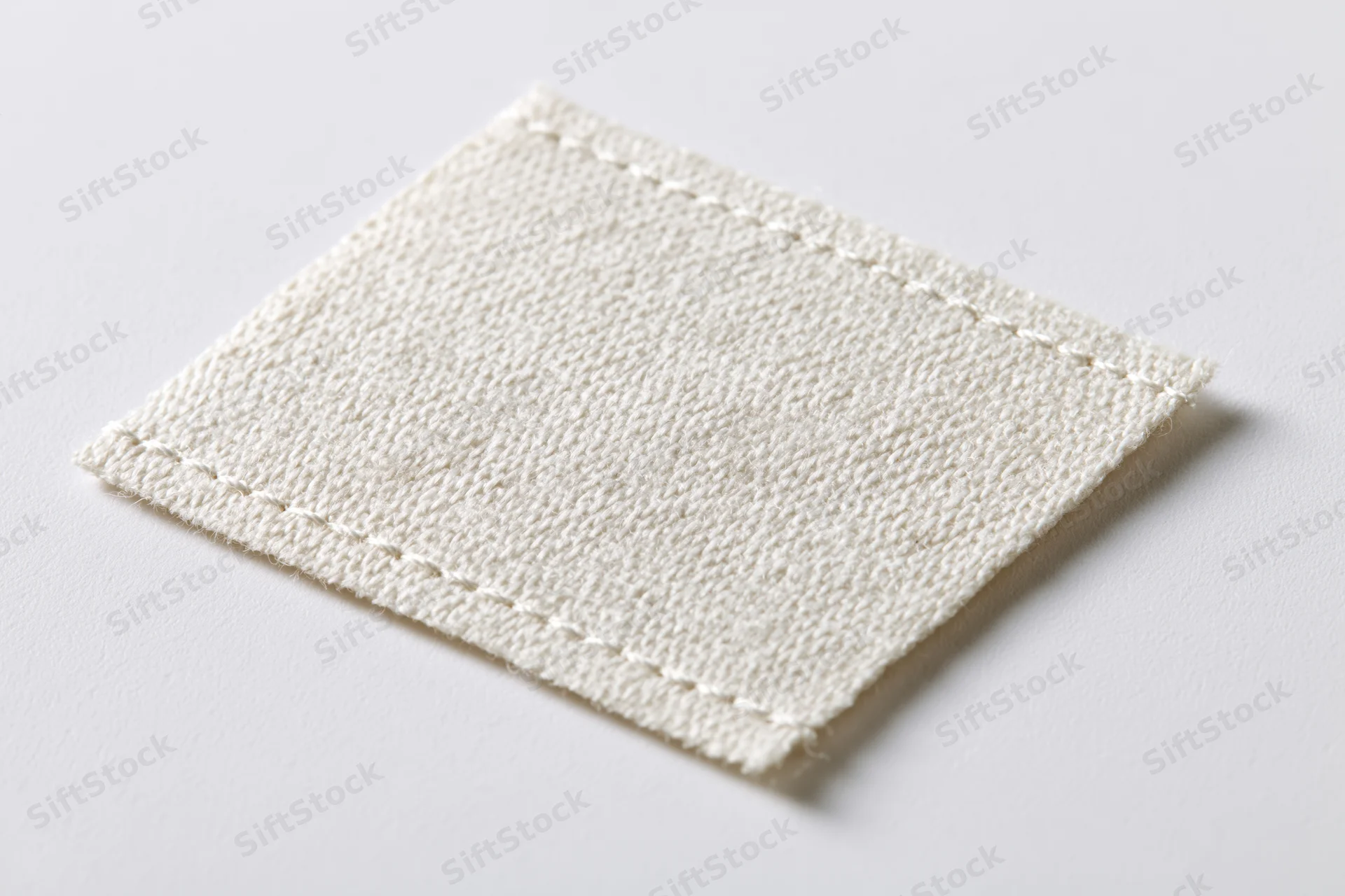 White fabric clothing label stitched at edges lying flat on plain surface