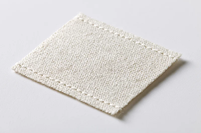 White fabric clothing label stitched at edges lying flat on plain surface