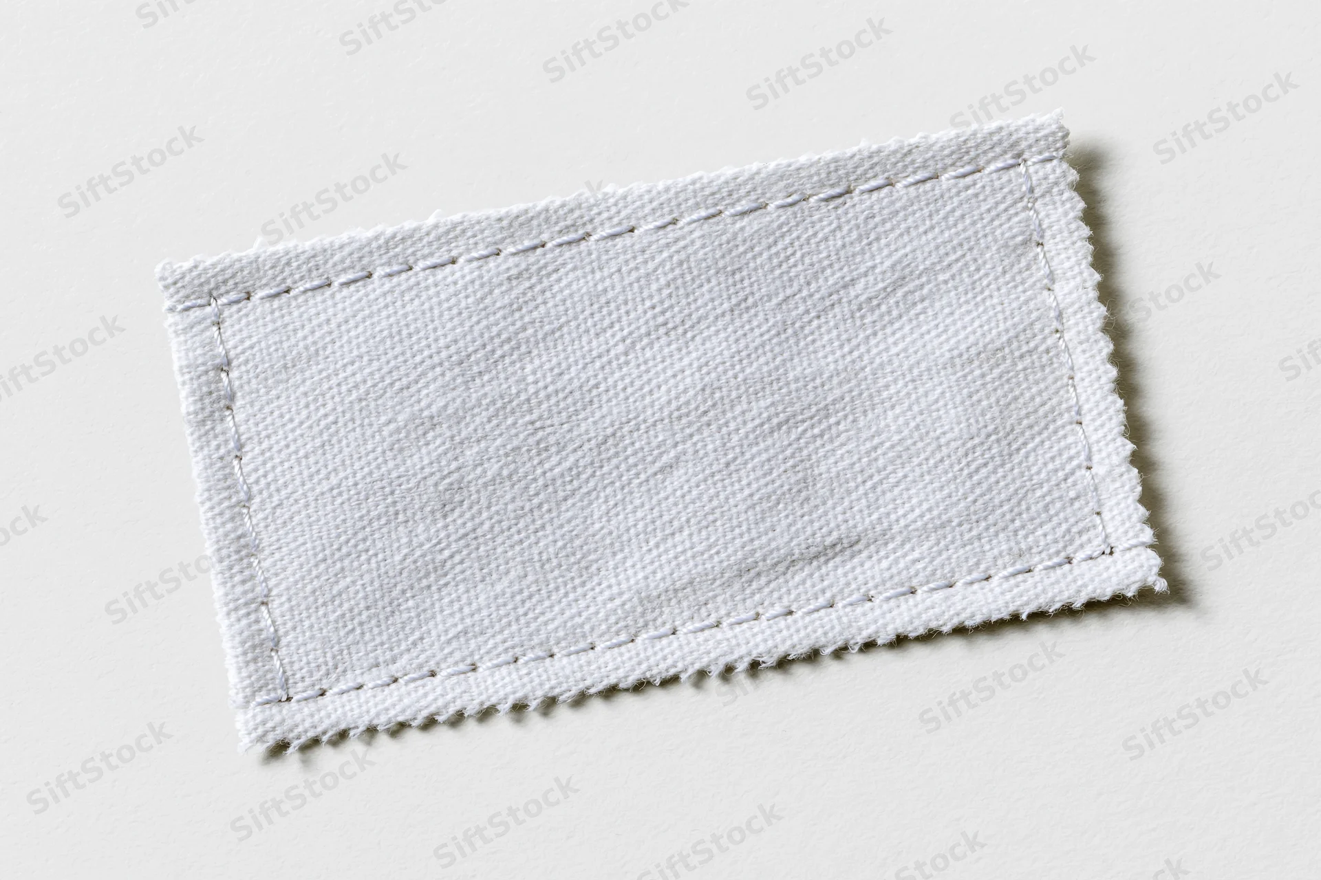 White fabric clothing label stitched with thread lying flat on plain surface