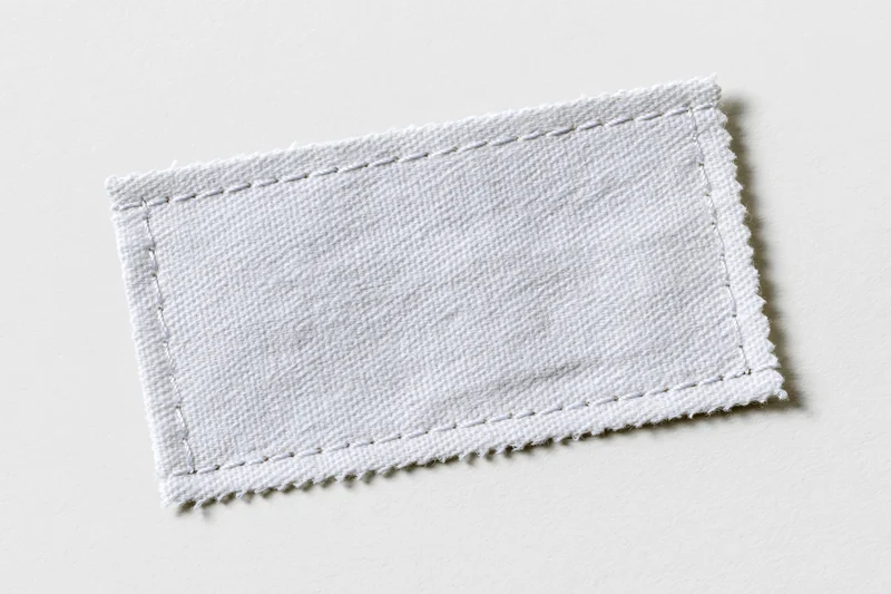 White fabric clothing label stitched with thread lying flat on plain surface