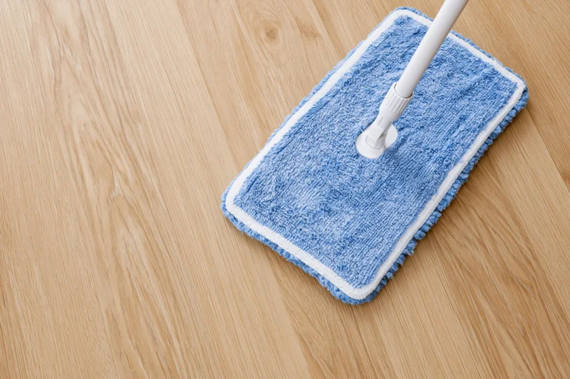 Blue microfiber mop head on wooden floor with white handle