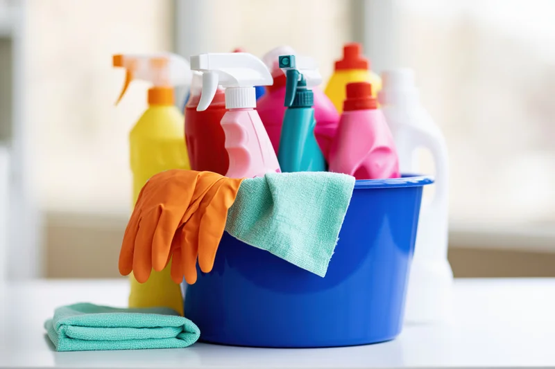 Blue plastic bucket filled with colorful cleaning supplies and gloves on a kitchen countertop