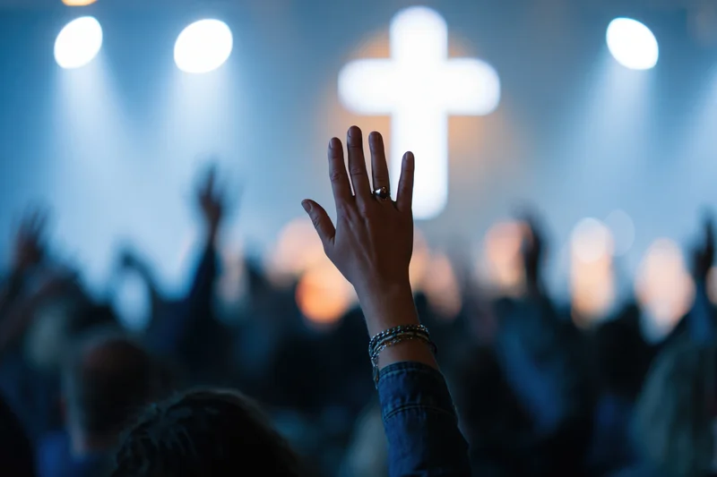 Hand raised in worship during church service with cross and stage lights in background