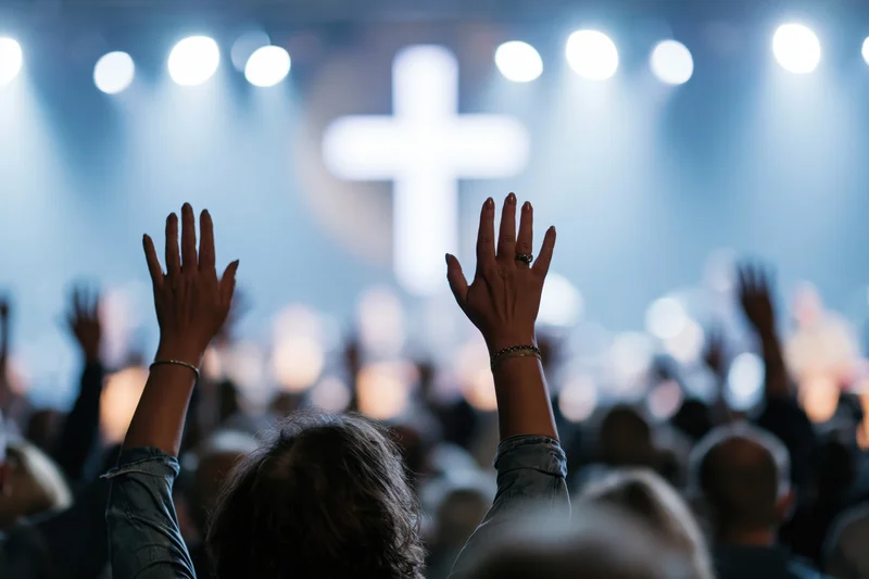Woman raising hands in worship at church service with cross and stage lights in background