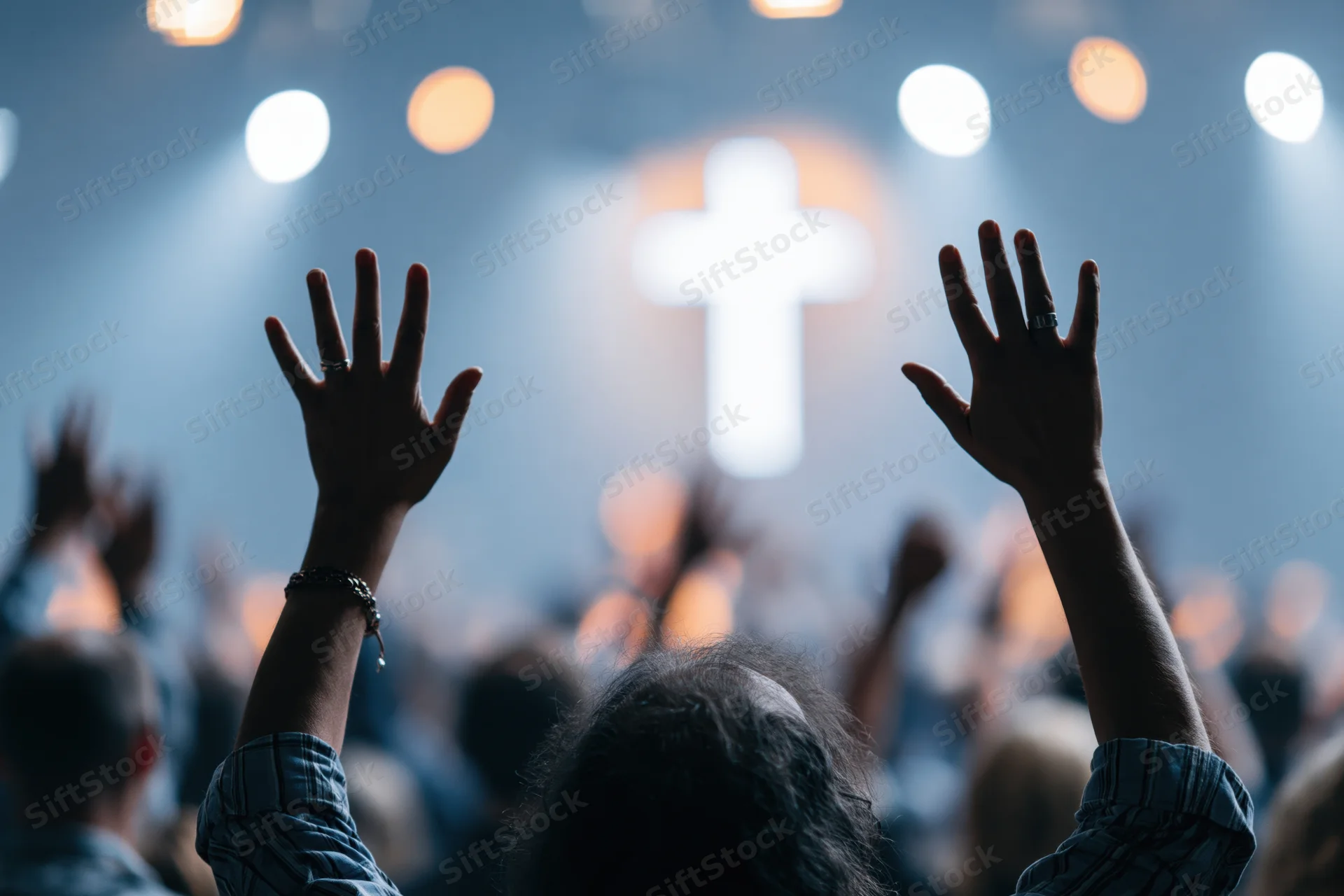 Congregation raising hands in worship at church service with illuminated cross and stage lights