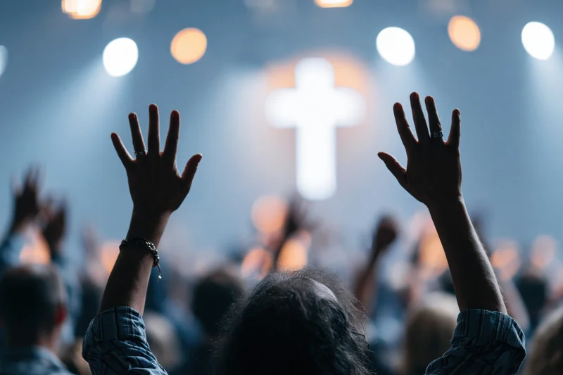 Congregation raising hands in worship at church service with illuminated cross and stage lights