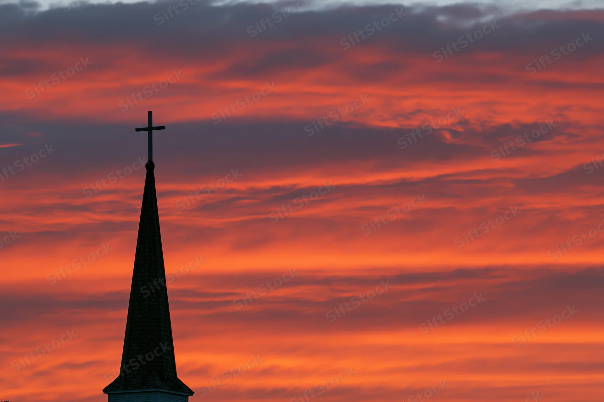 Church steeple with cross silhouetted against vibrant orange sunset sky