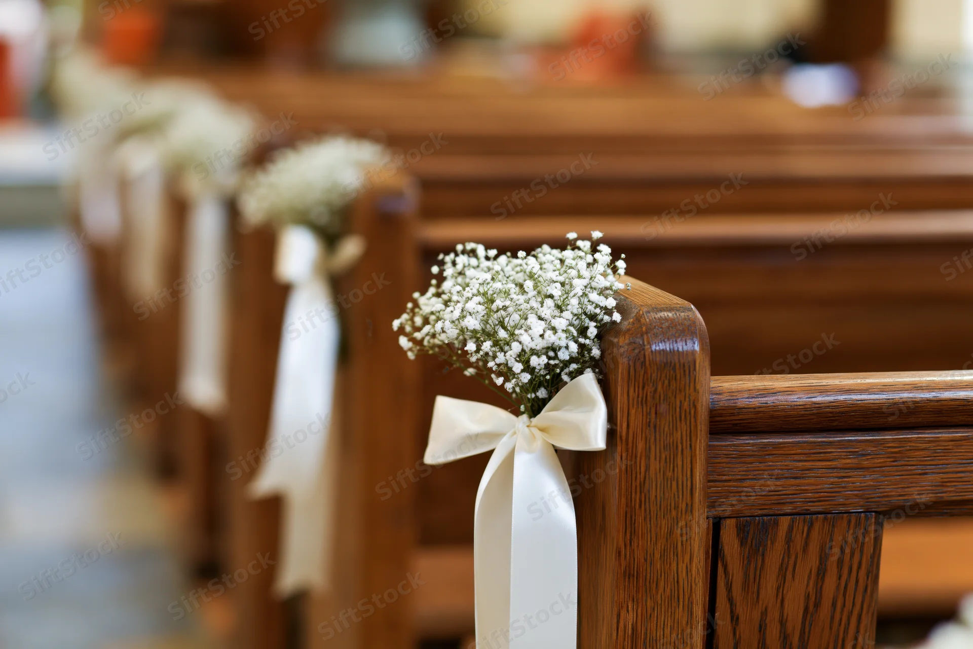 Wooden church pews decorated with baby's-breath flowers and white ribbons along the aisle for a wedding ceremony