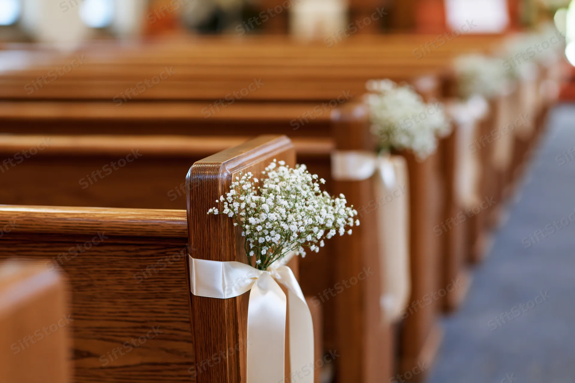 Wooden church pews lined with baby's breath flowers and cream ribbons along a central aisle for a wedding ceremony
