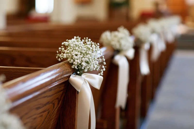 White baby's-breath flowers tied with ribbons on wooden church pews along an aisle