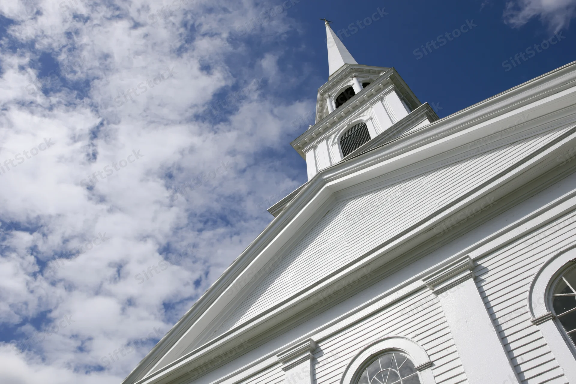 White clapboard church with tall steeple under blue sky with scattered clouds