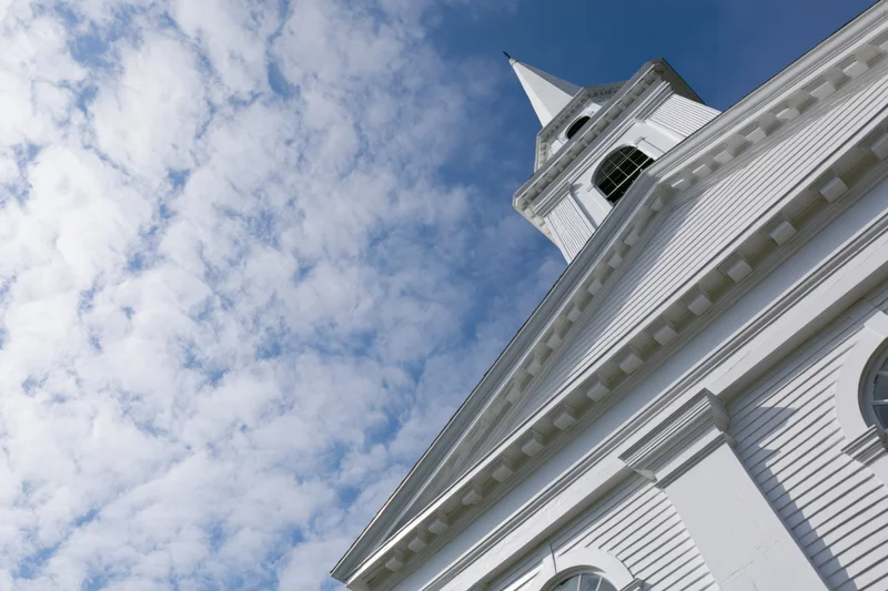 Low angle view of white clapboard church with tall steeple against blue sky with clouds