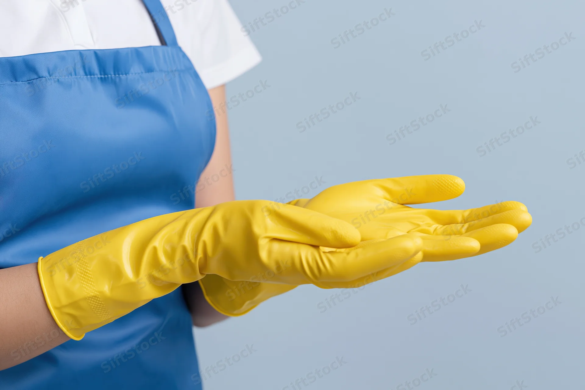 Woman in blue apron wearing yellow rubber gloves with hands extended in front of her