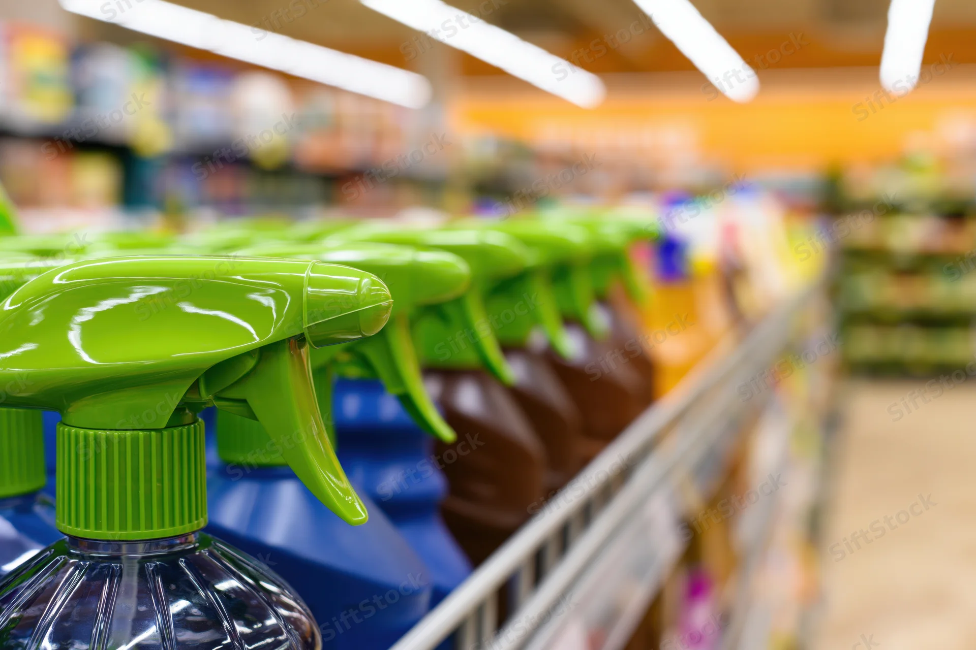 Cleaning spray bottles with bright green trigger nozzles lined up on supermarket shelves