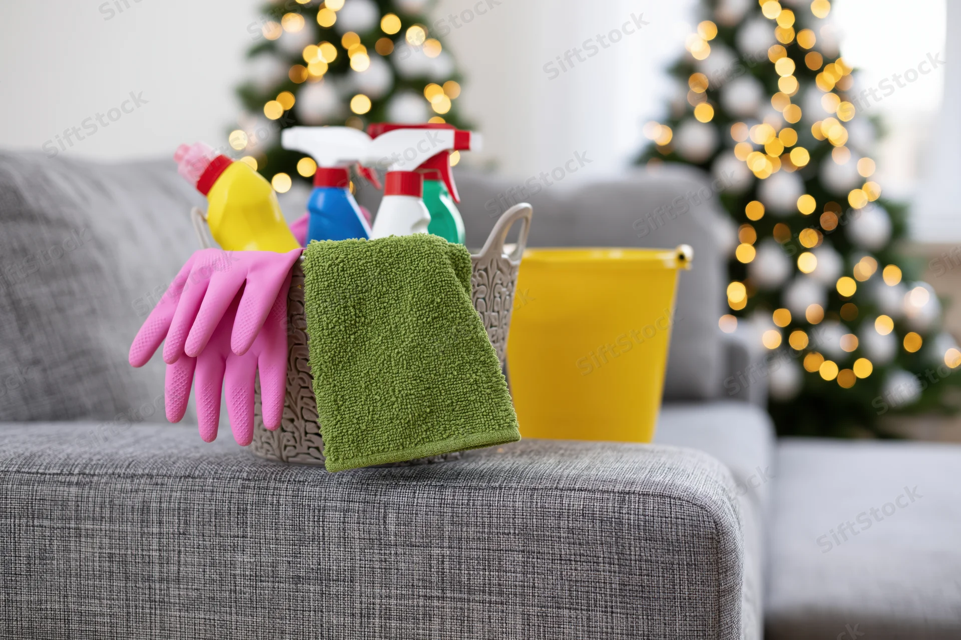 Cleaning supplies basket on grey sofa arm with christmas trees in background
