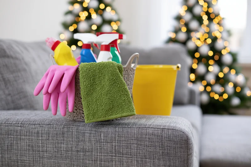 Cleaning supplies basket on grey sofa arm with christmas trees in background