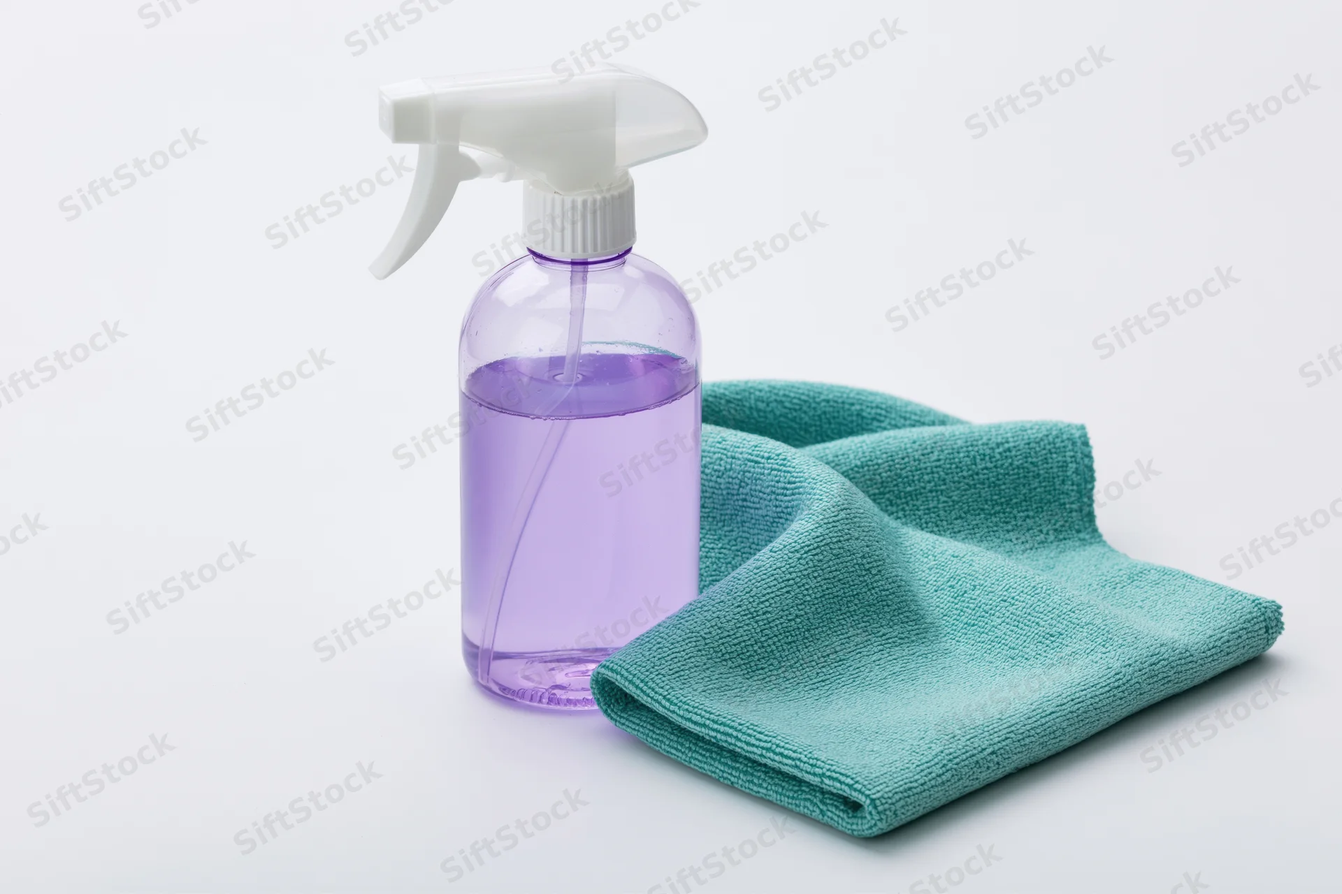 Clear plastic spray bottle with purple liquid and teal microfiber cloth on white background