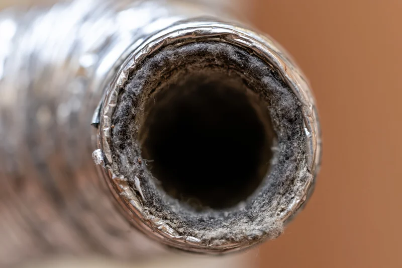 Close-up view looking directly into the open end of a dusty metal ventilation pipe