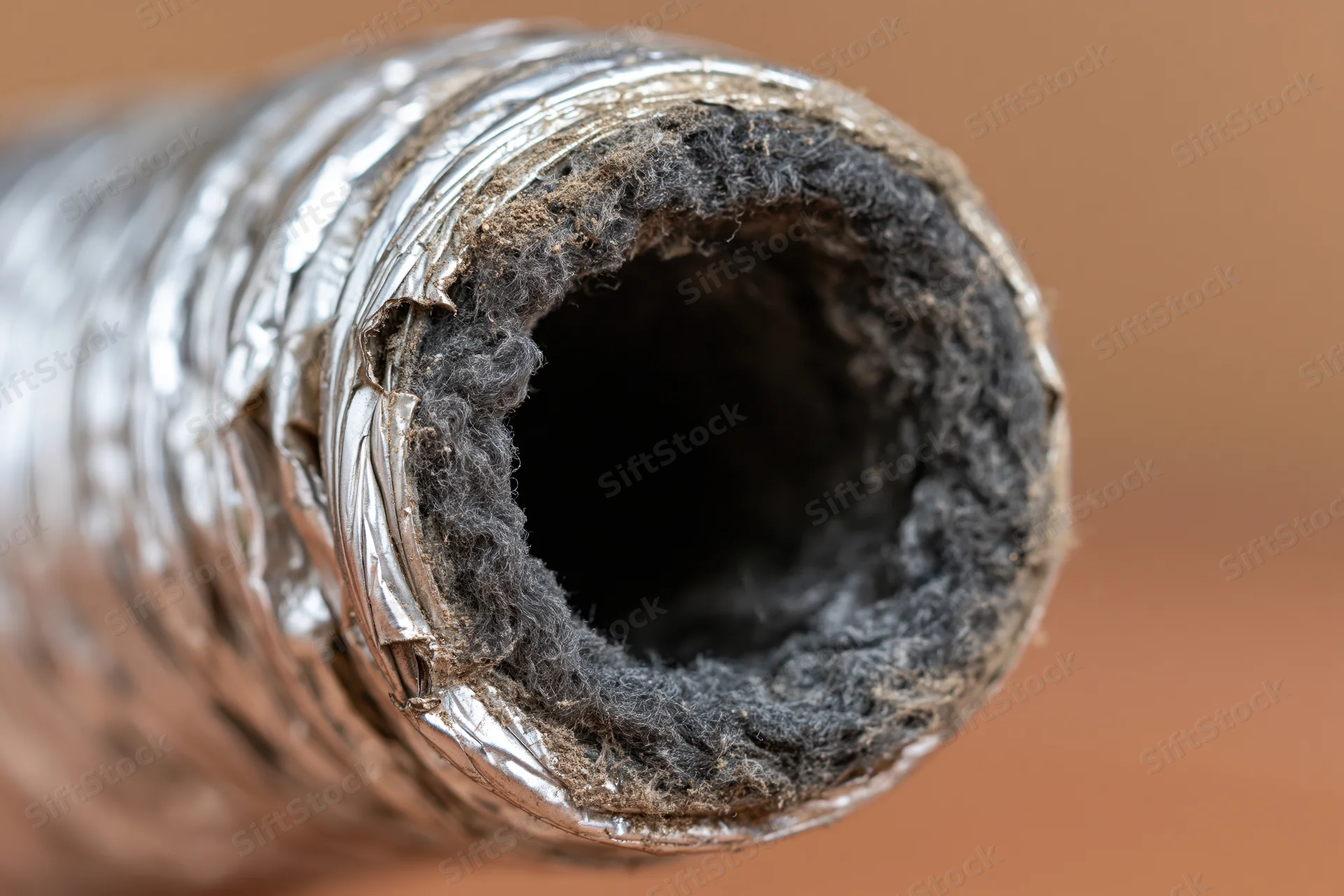 Close-up view looking directly into the open end of a flexible ventilation duct with exposed insulation and foil lining