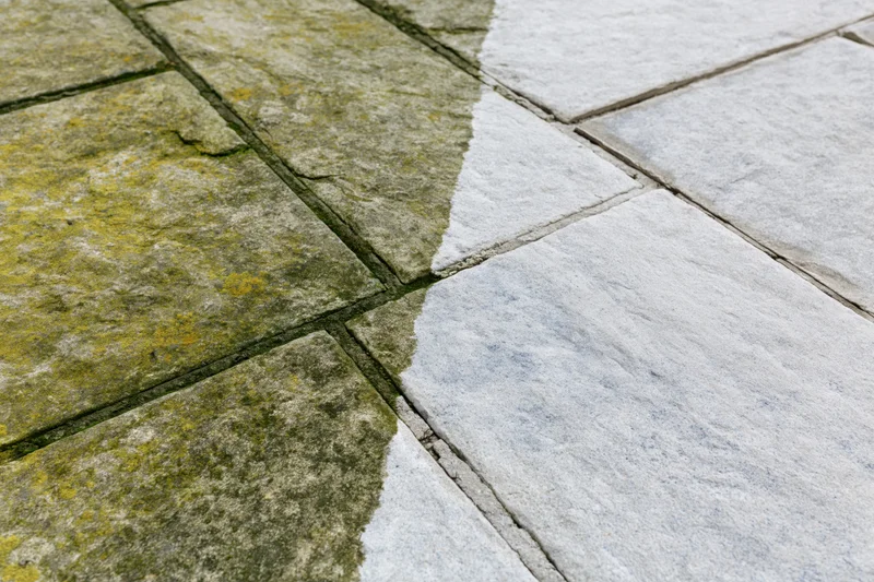Stone patio surface showing before and after cleaning comparison with moss and grime on one side and clean white stone on the other
