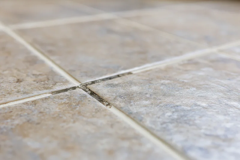 Close-up of ceramic floor tiles with stained grout lines in a home interior