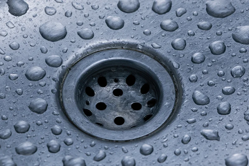 Close-up of a stainless steel sink drain with water droplets on its surface