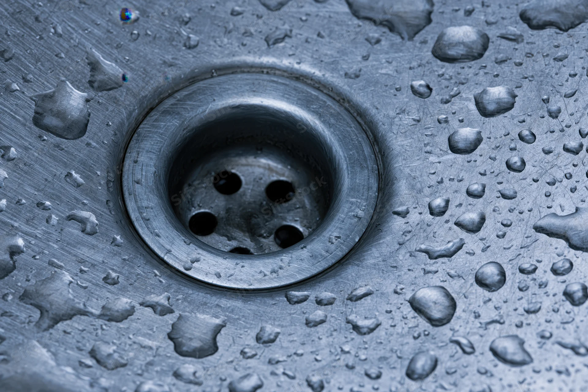 Close-up of a stainless steel sink drain with water droplets on its surface