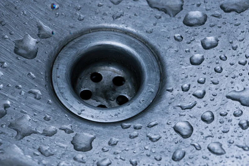 Close-up of a stainless steel sink drain with water droplets on its surface