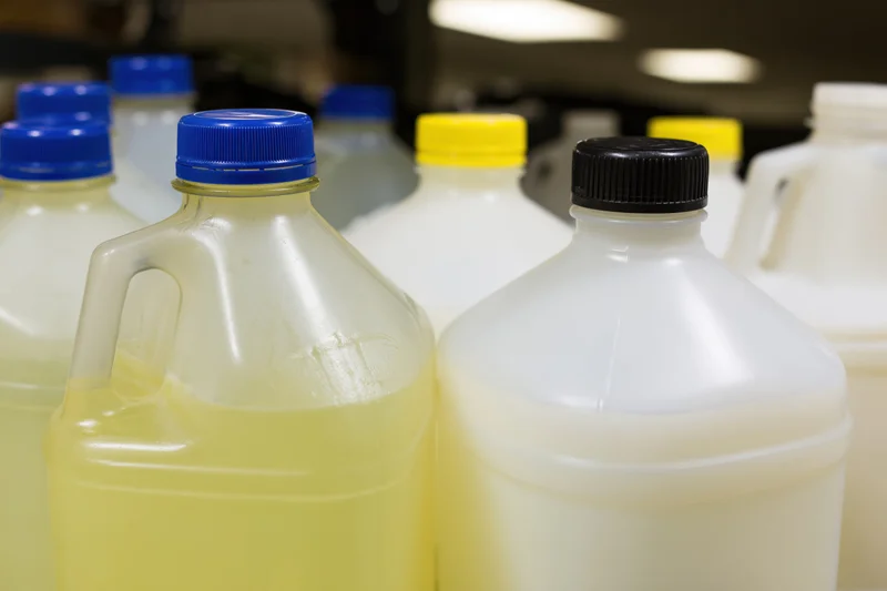 Multiple one-gallon plastic jugs grouped together in a storage area