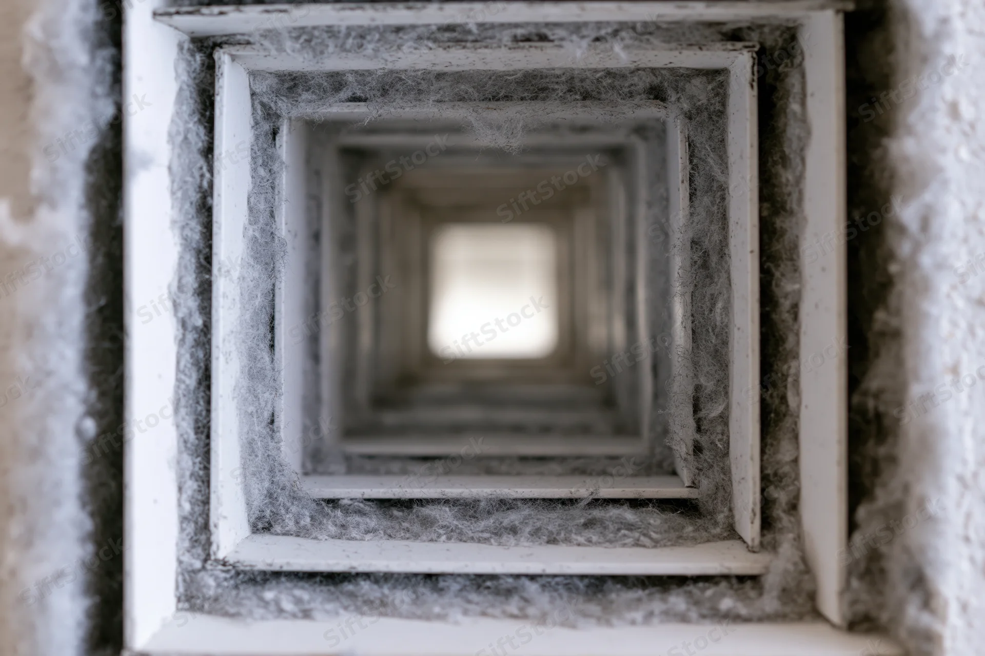 Close-up view looking up into a square ceiling air duct lined with fibrous insulation