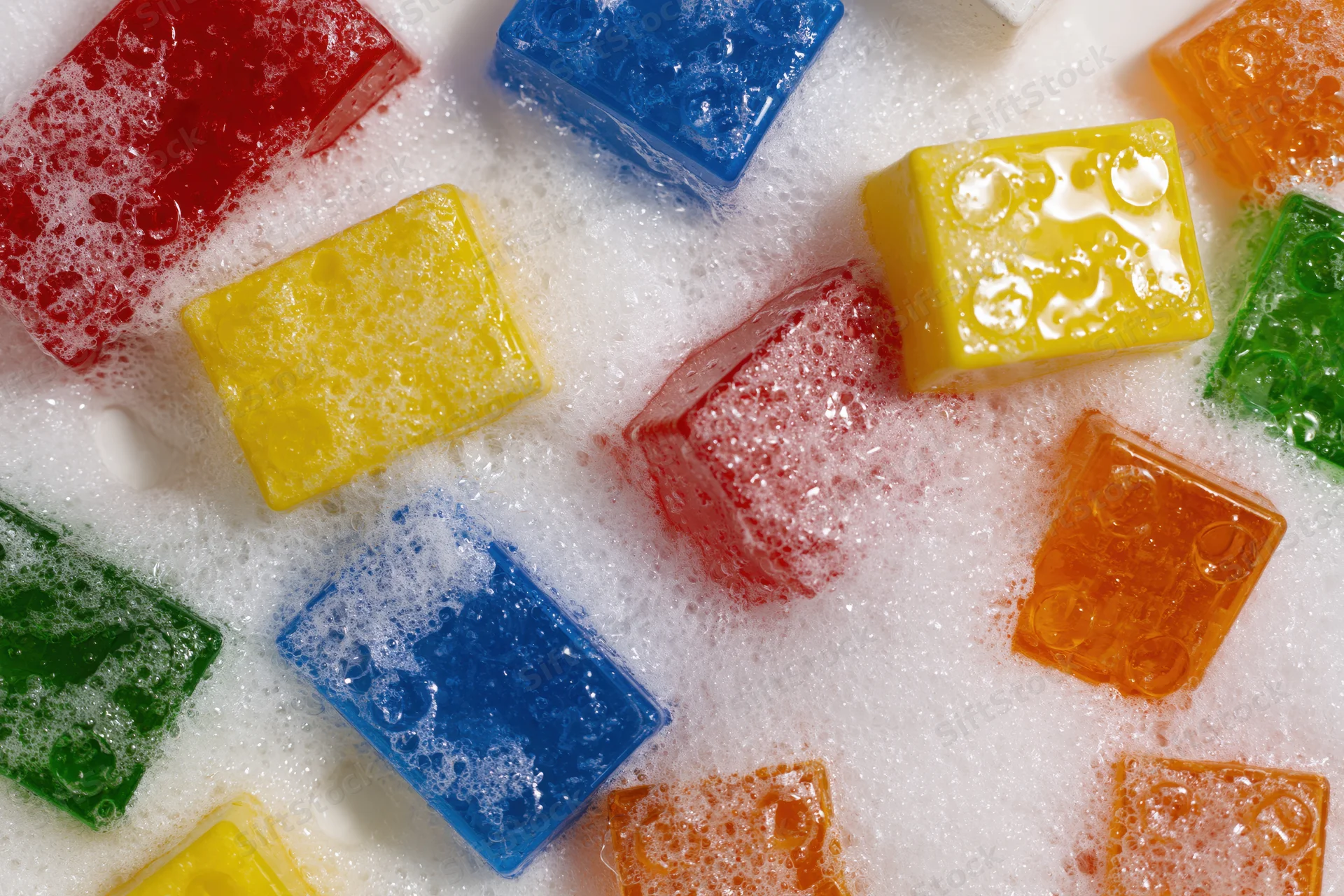 Colorful plastic building blocks floating in soapy foam bath water