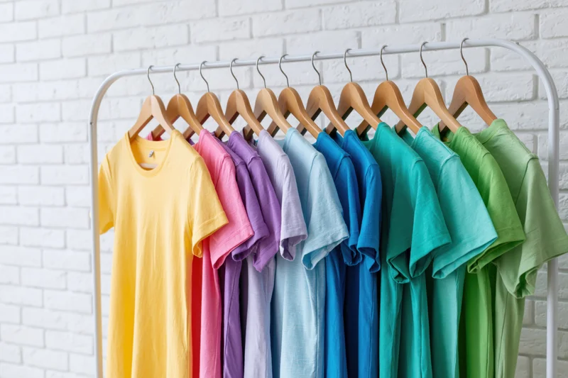 Colorful tshirts arranged in rainbow order on a white brick wall rack